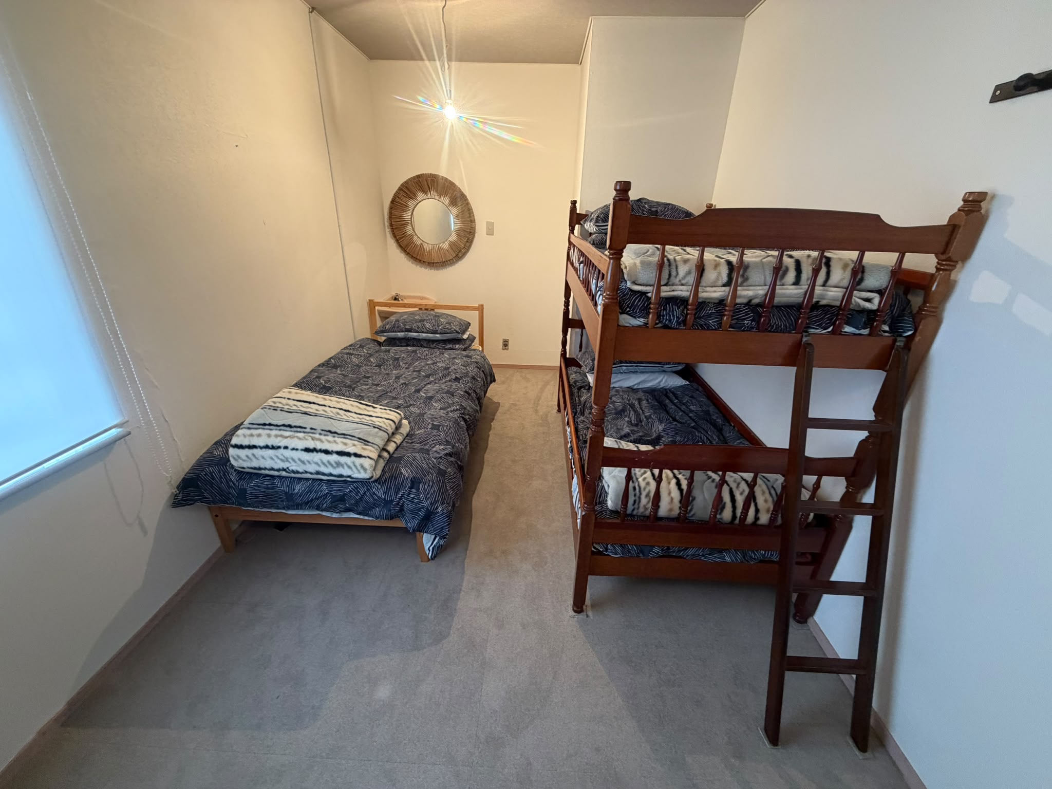 Bedroom with twin bed, bunk bed, and woven sunburst mirror